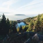 Bergsee mit Hotelanlage inmitten eines Tannenwaldes bei Morgenlicht – Symbolbild für Leisure-Destinationen im Sommer 2025